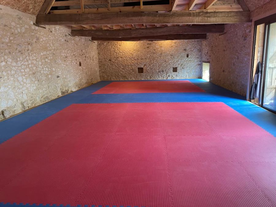 Le dojo aménagé en Dordogne : murs en pierre, charpente apparente et tatamis